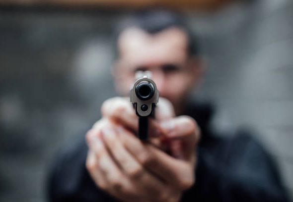 A man is pointing a gun directly at the lens.